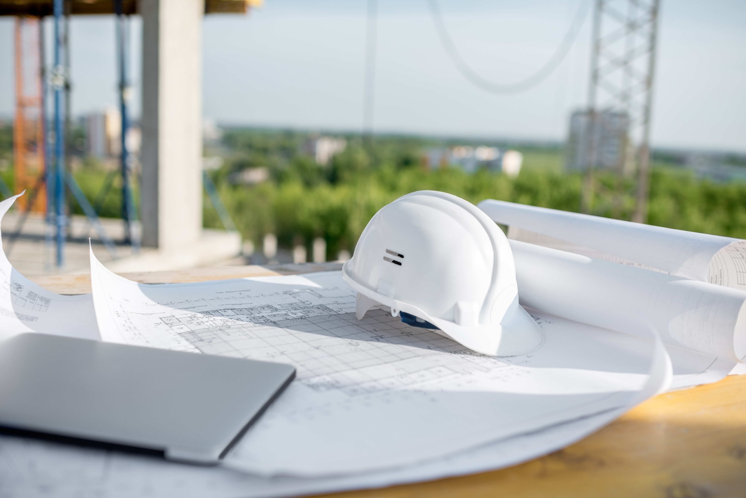 Capacete branco sobre plantas e projetos de construção em canteiro de obras