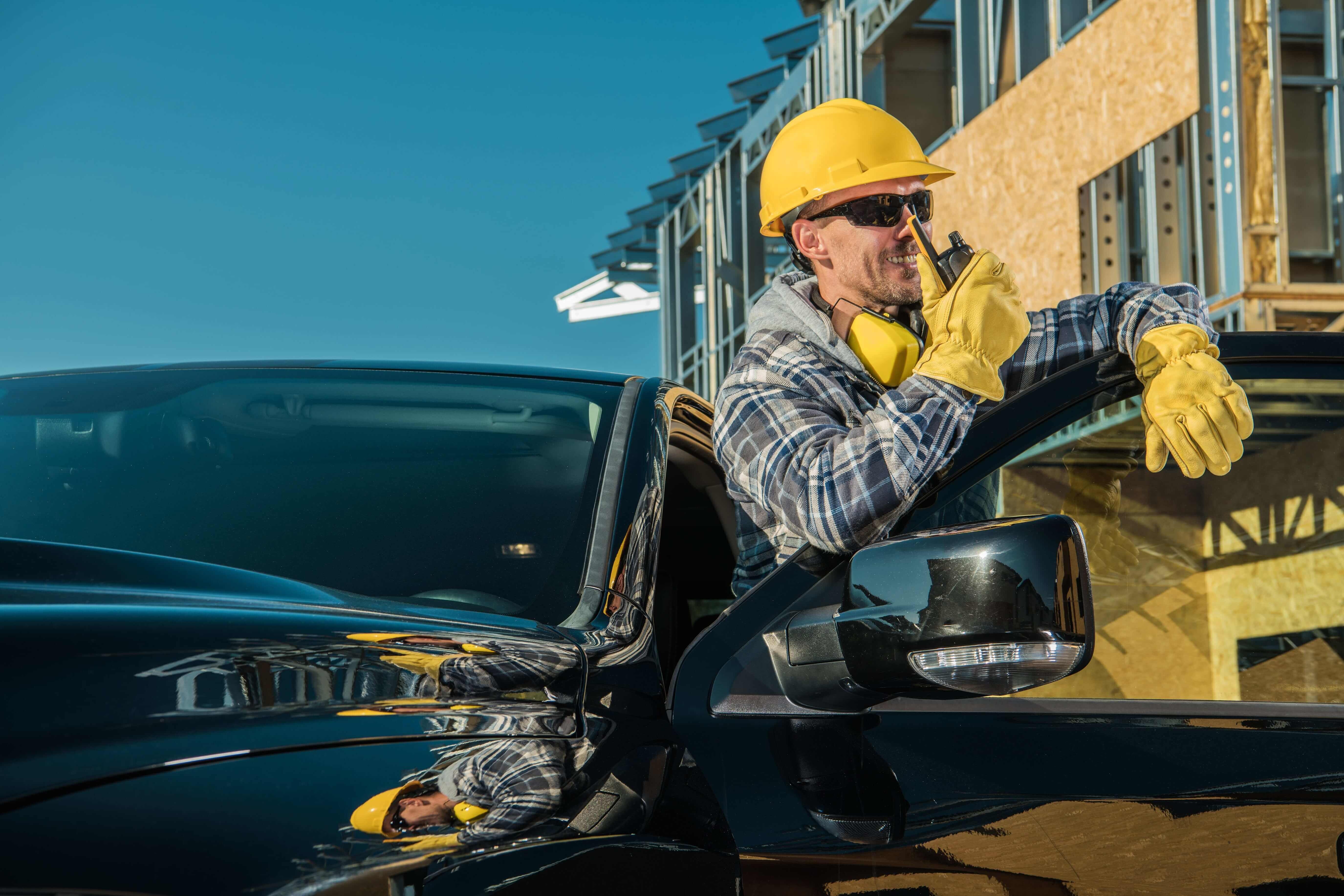 Empreiteiro brasileiro feliz com capacete amarelo saindo do carro em canteiro de obras